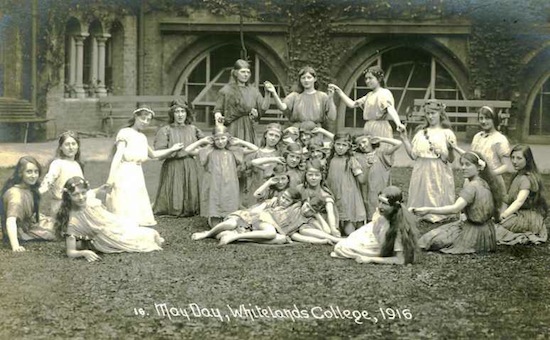 group of women and young girls outside an old brick building in greek costumes